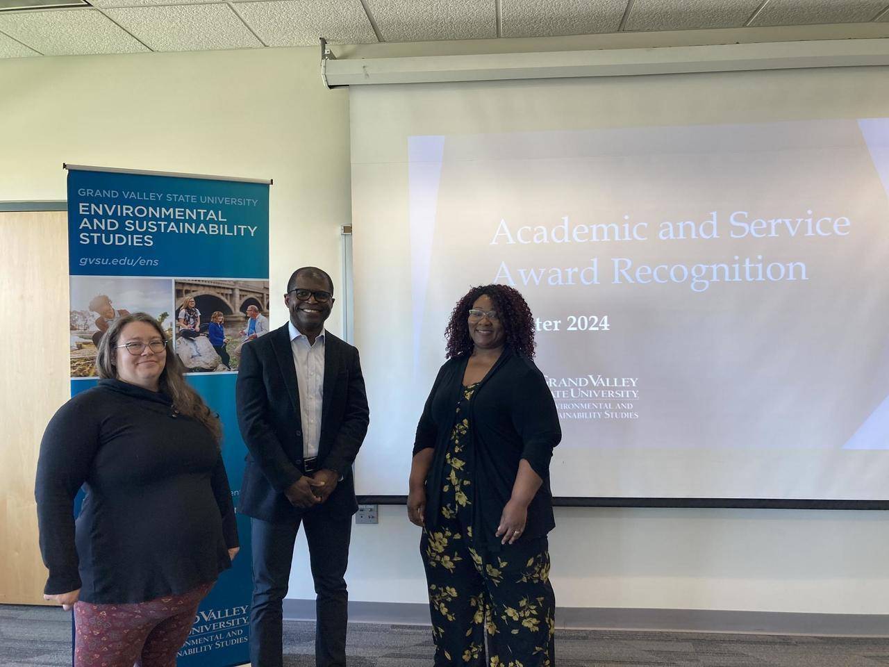 A photo of three professors standing in front of a projector screen
